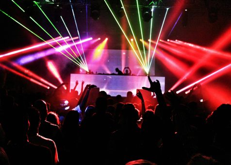 Energetic nightclub scene with laser lights and a lively crowd dancing to EDM music.